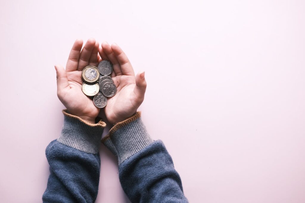 Close-up of hands in sweater holding various coins, indicating savings and finance on a white background.