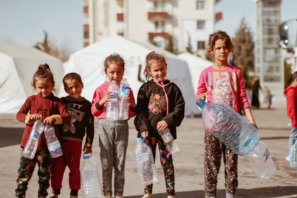Group of children holding plastic bottles in a temporary urban setting in Türkiye.