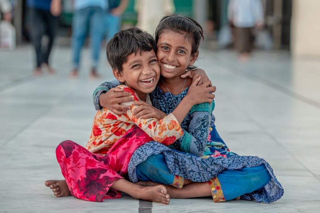 Two smiling children sit and hug outdoors, exuding warmth and joy.