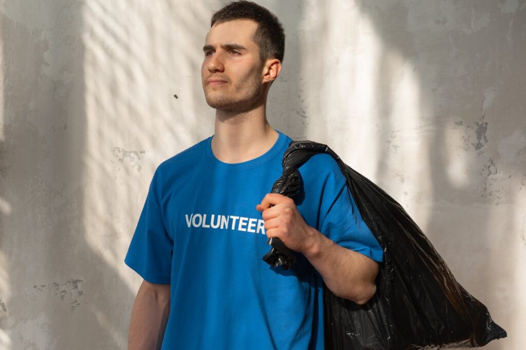 A young male volunteer holding a garbage bag indoors, promoting environmental protection.